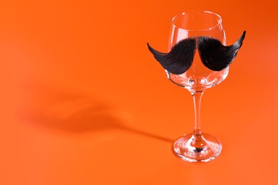 Photo of Man's face made of artificial mustache and wine glass on orange background. Space for text