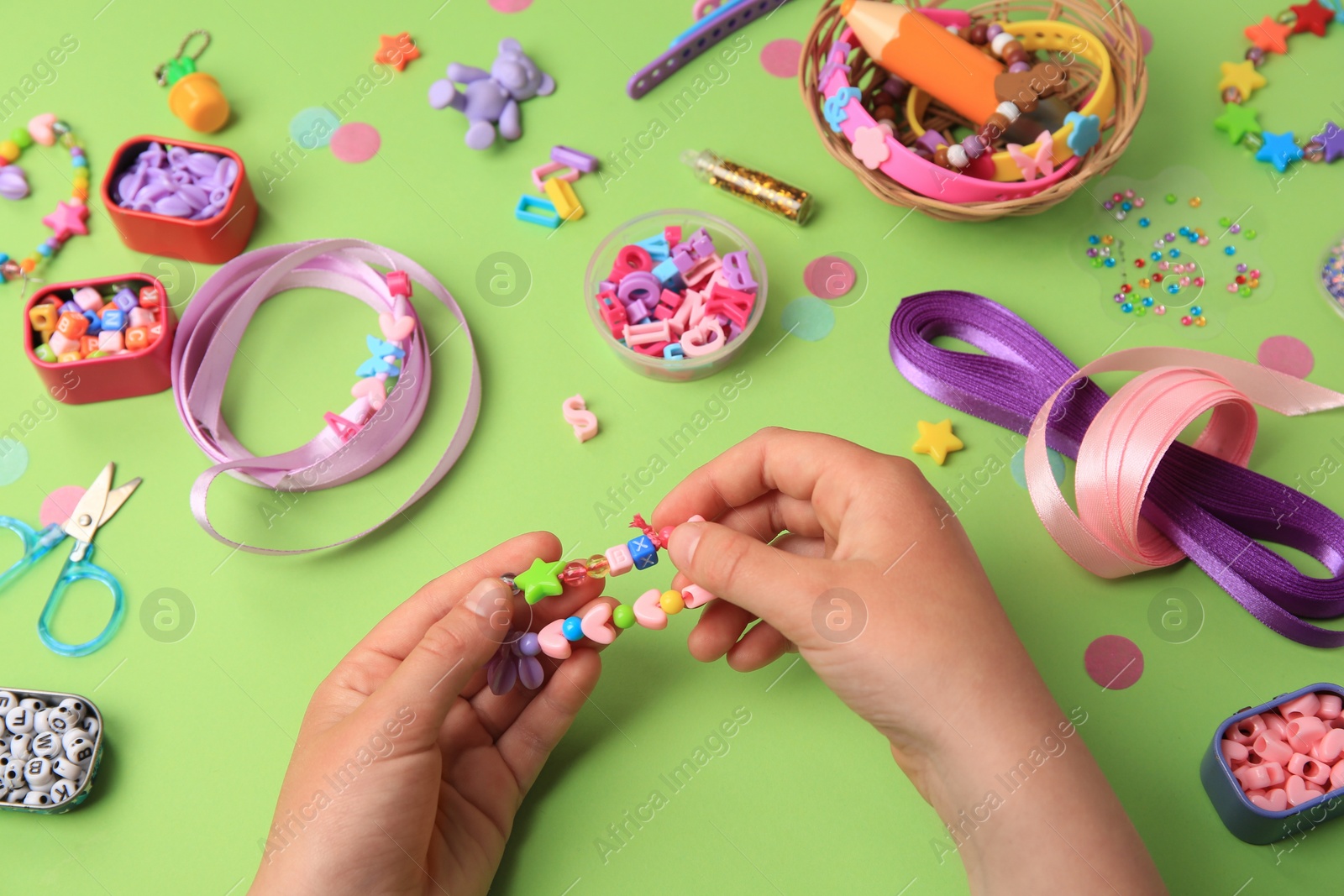 Photo of Child making beaded jewelry and different supplies on green background, above view. Handmade accessories