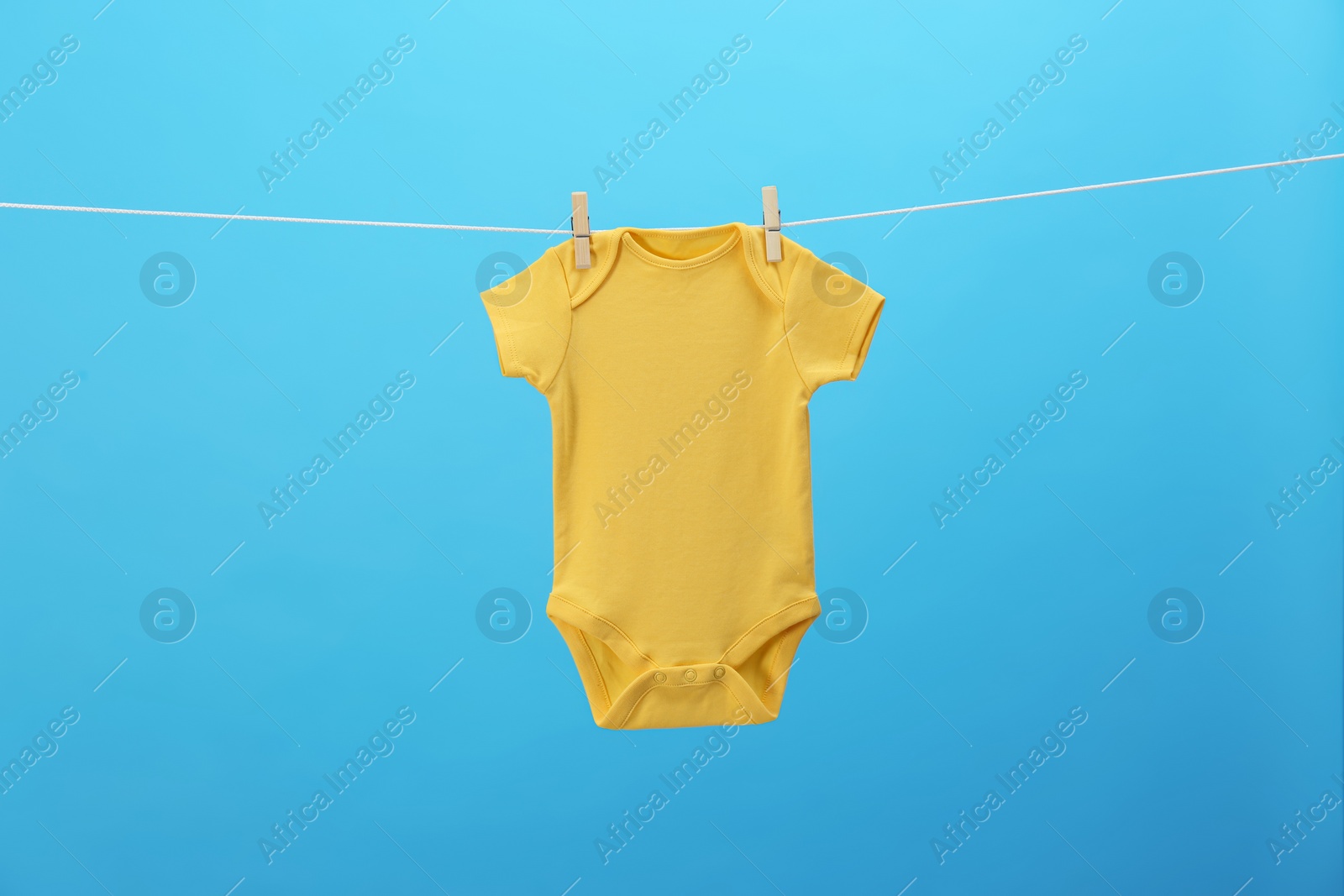 Photo of Baby onesie hanging on clothes line against blue background. Laundry day