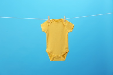 Photo of Baby onesie hanging on clothes line against blue background. Laundry day