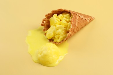 Photo of Melted ice cream in wafer cone on pale yellow background