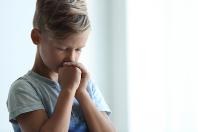 Photo of Little boy with hands clasped together for prayer on light background. Space for text