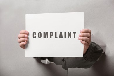 Image of Man holding card with word Complaint through hole in paper, closeup