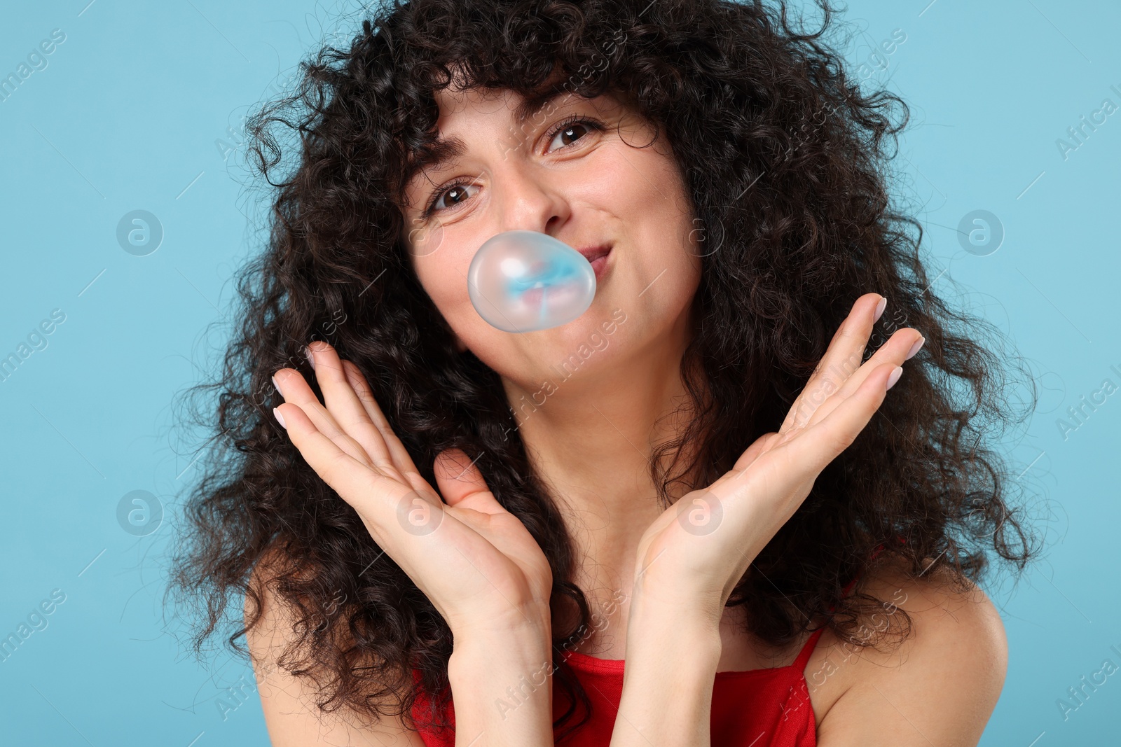 Photo of Beautiful young woman blowing bubble gum on light blue background