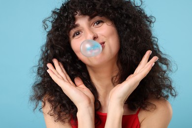 Photo of Beautiful young woman blowing bubble gum on light blue background