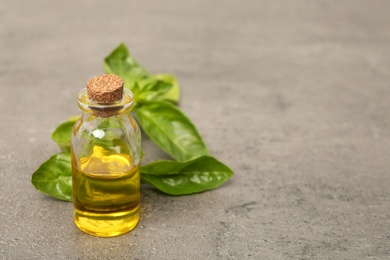 Photo of Glass bottle of basil oil with leaves and space for text on table