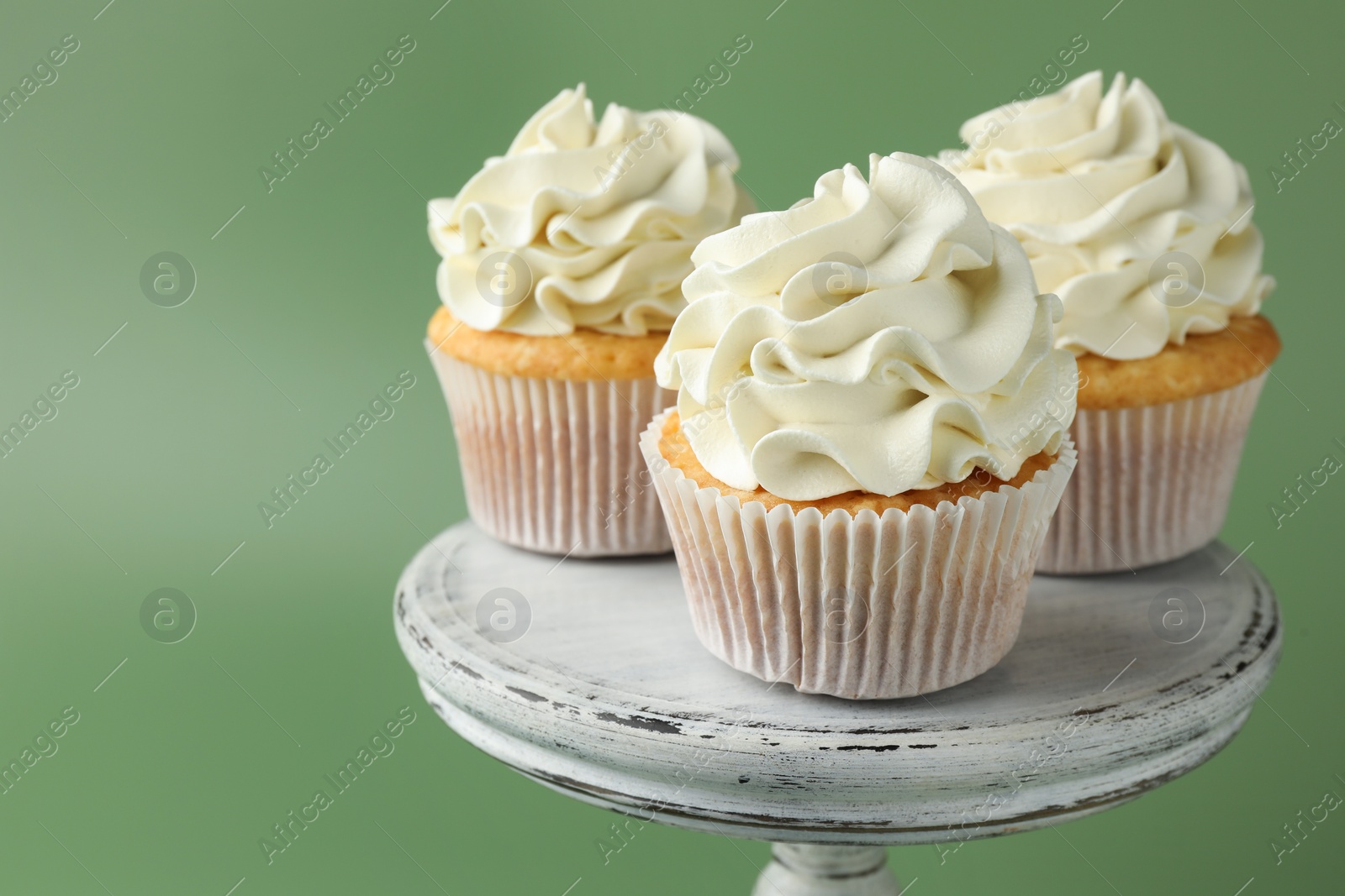 Photo of Tasty vanilla cupcakes with cream on green background, closeup