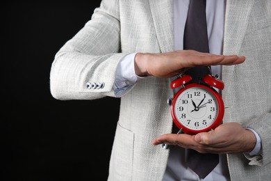 Photo of Businessman holding alarm clock on black background, closeup. Time management