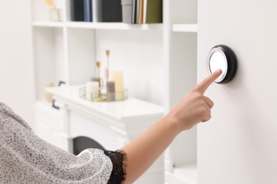 Photo of Woman adjusting thermostat on white wall indoors, closeup. Smart home system