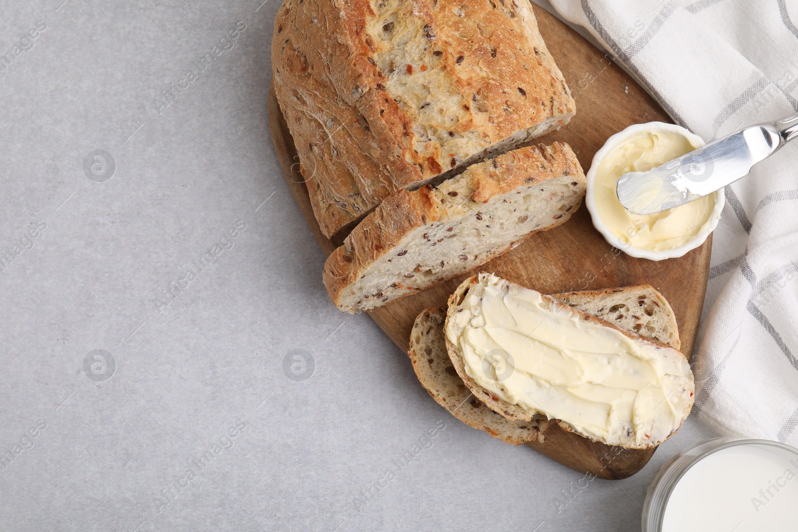 Photo of Tasty bread with butter, knife and milk in glass on gray table, flat lay. Space for text