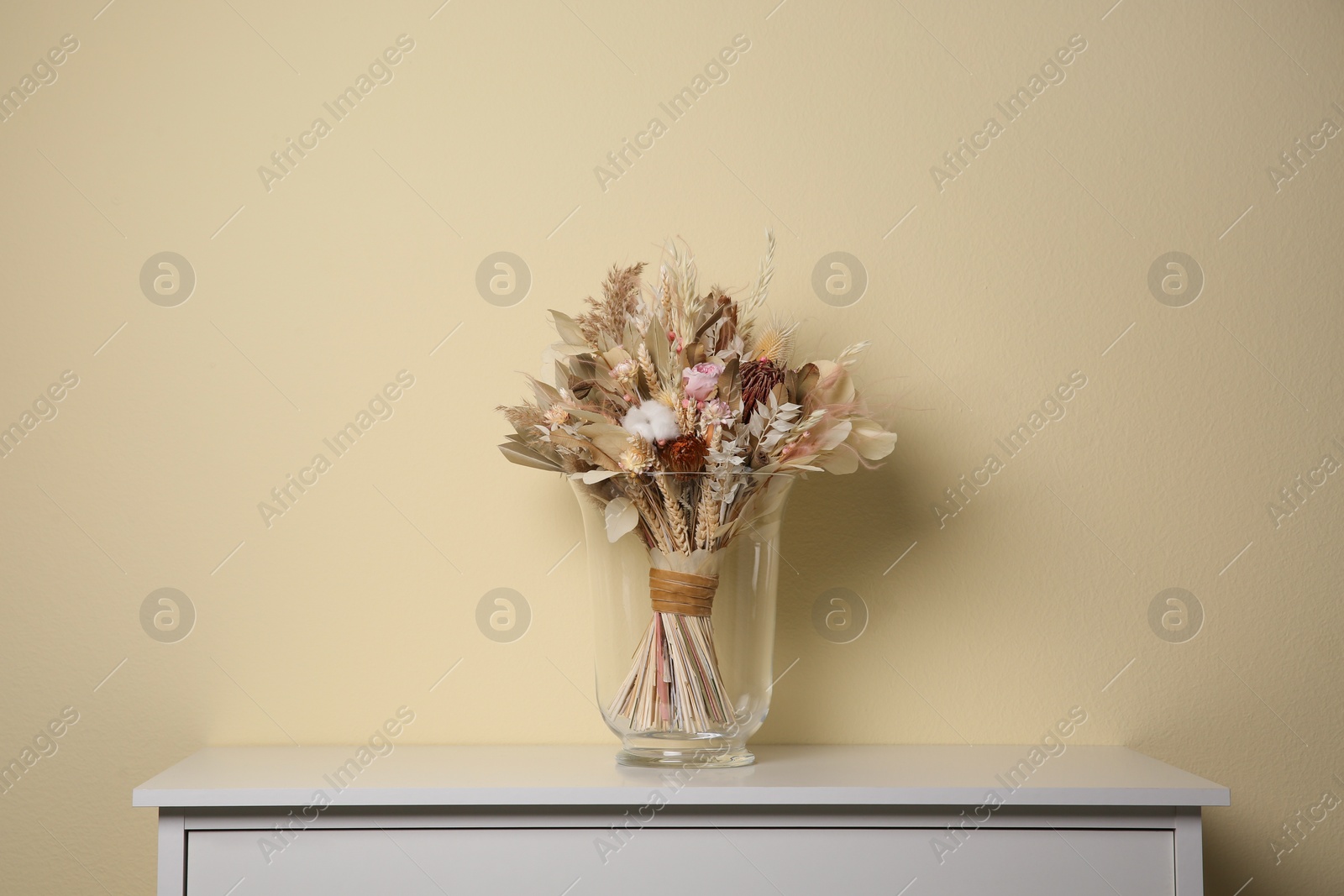 Photo of Beautiful dried flower bouquet in glass vase on white table near beige wall