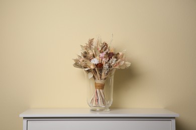 Photo of Beautiful dried flower bouquet in glass vase on white table near beige wall