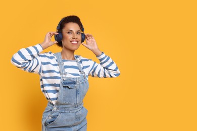 Photo of Happy young woman in headphones dancing on orange background. Space for text