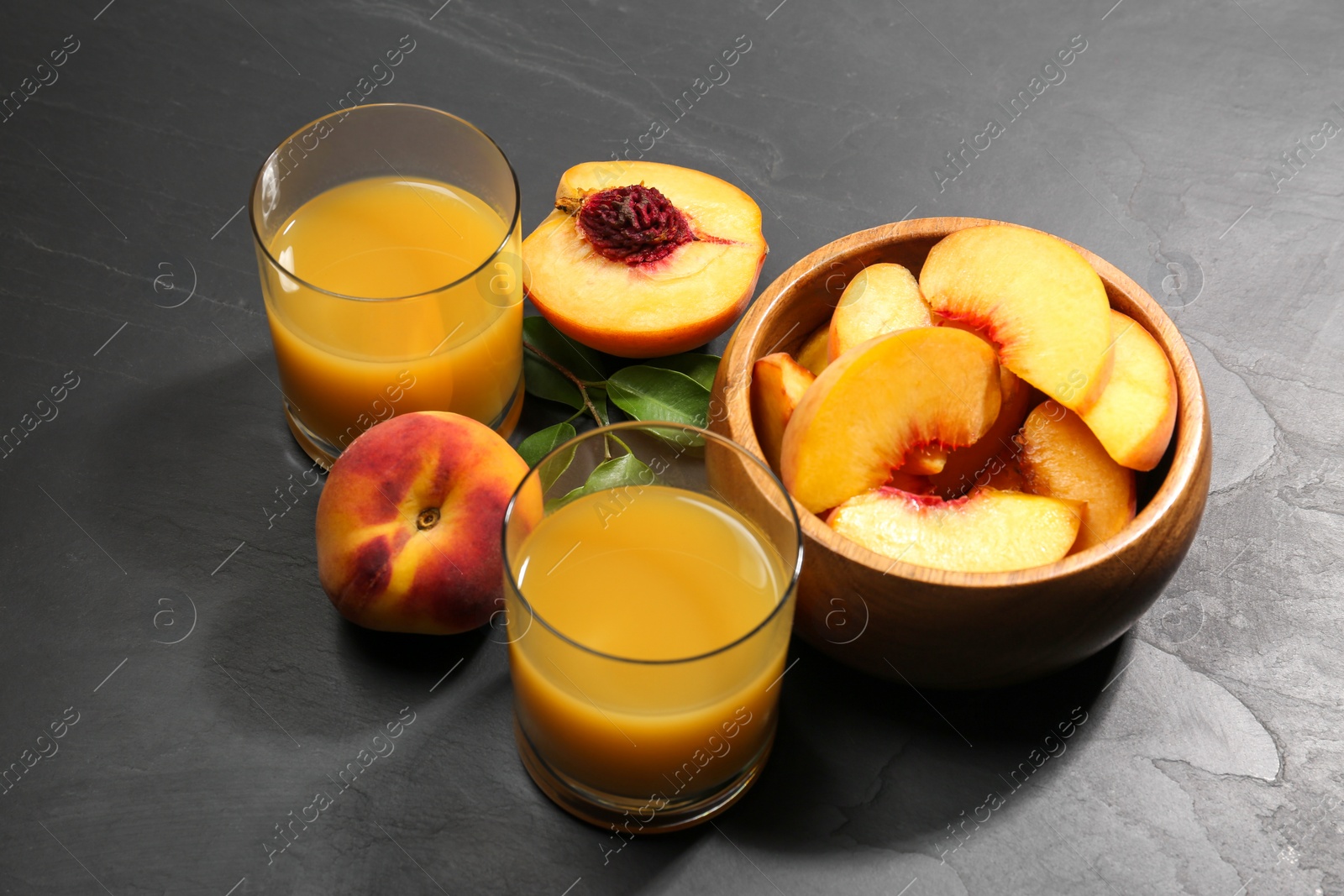 Photo of Glasses of delicious peach juice, fresh fruits and leaves on black table