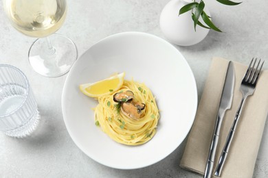 Photo of Tasty capellini with mussels and lemon served on light grey table, above view. Exquisite presentation of pasta dish