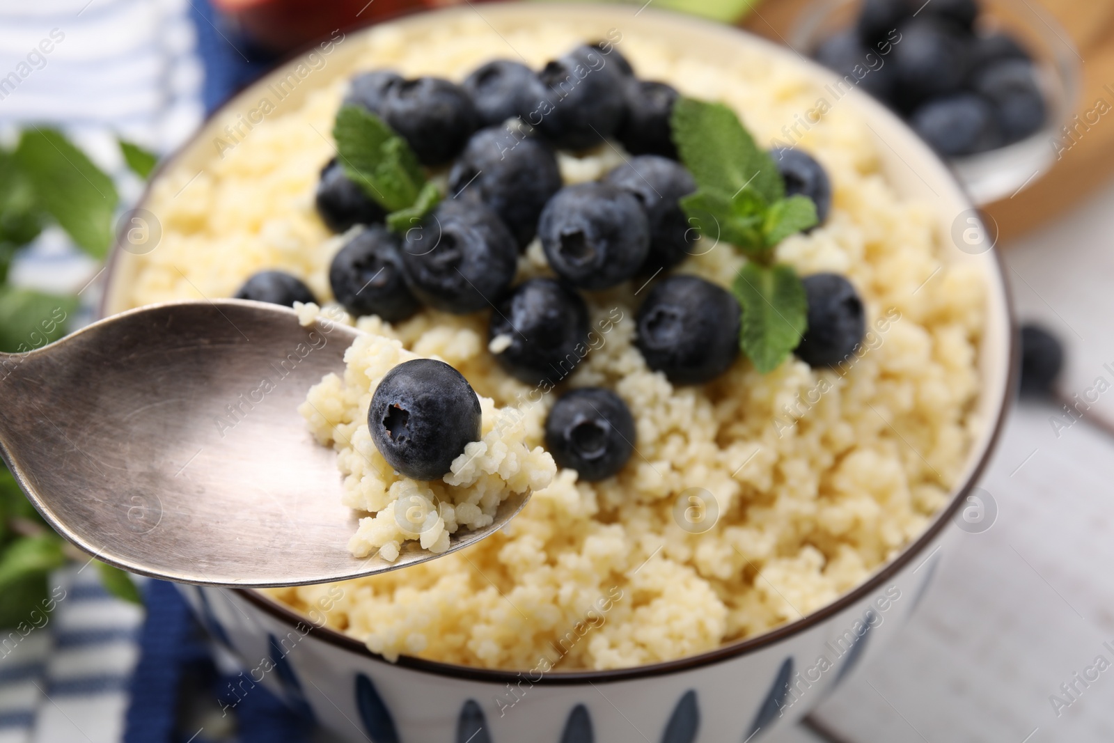 Photo of Eating tasty couscous with blueberries and mint from bowl, closeup