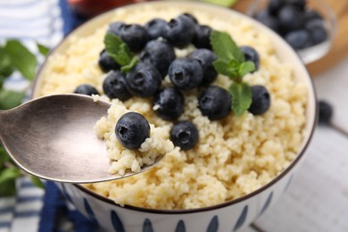 Eating tasty couscous with blueberries and mint from bowl, closeup