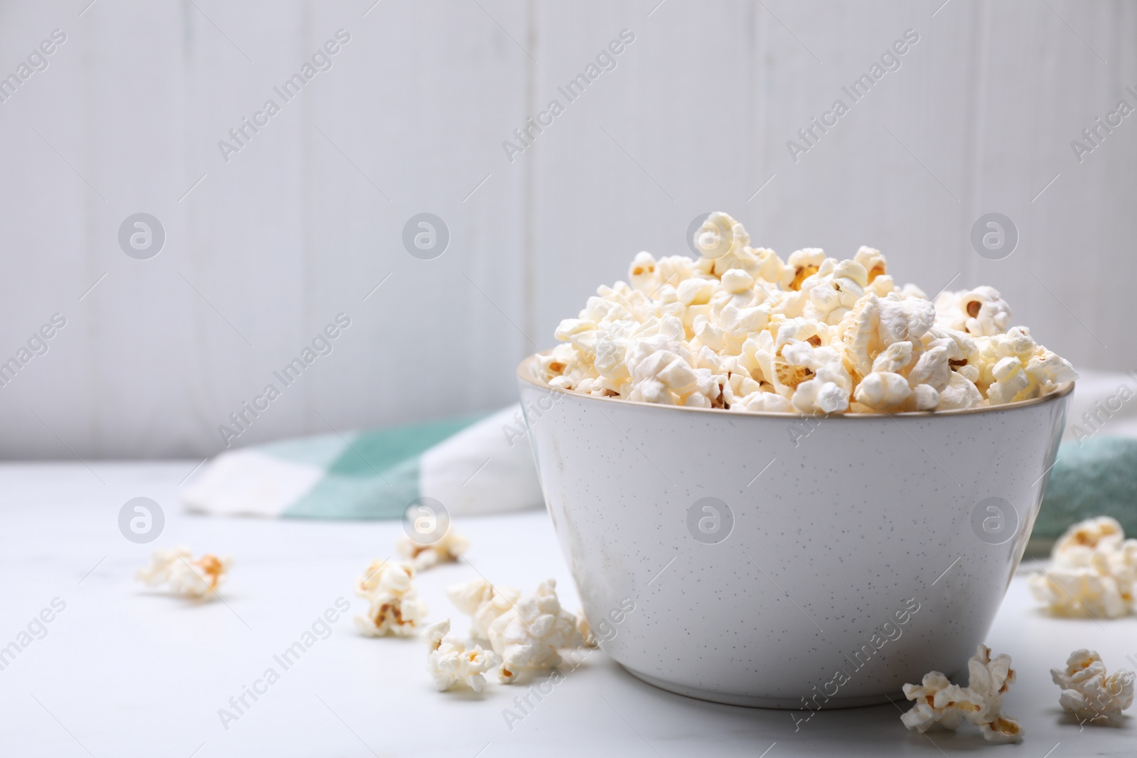 Photo of Bowl of tasty popcorn on white table, space for text