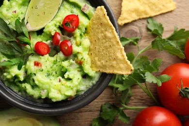 Photo of Delicious guacamole with nachos chips and ingredients on wooden table, flat lay