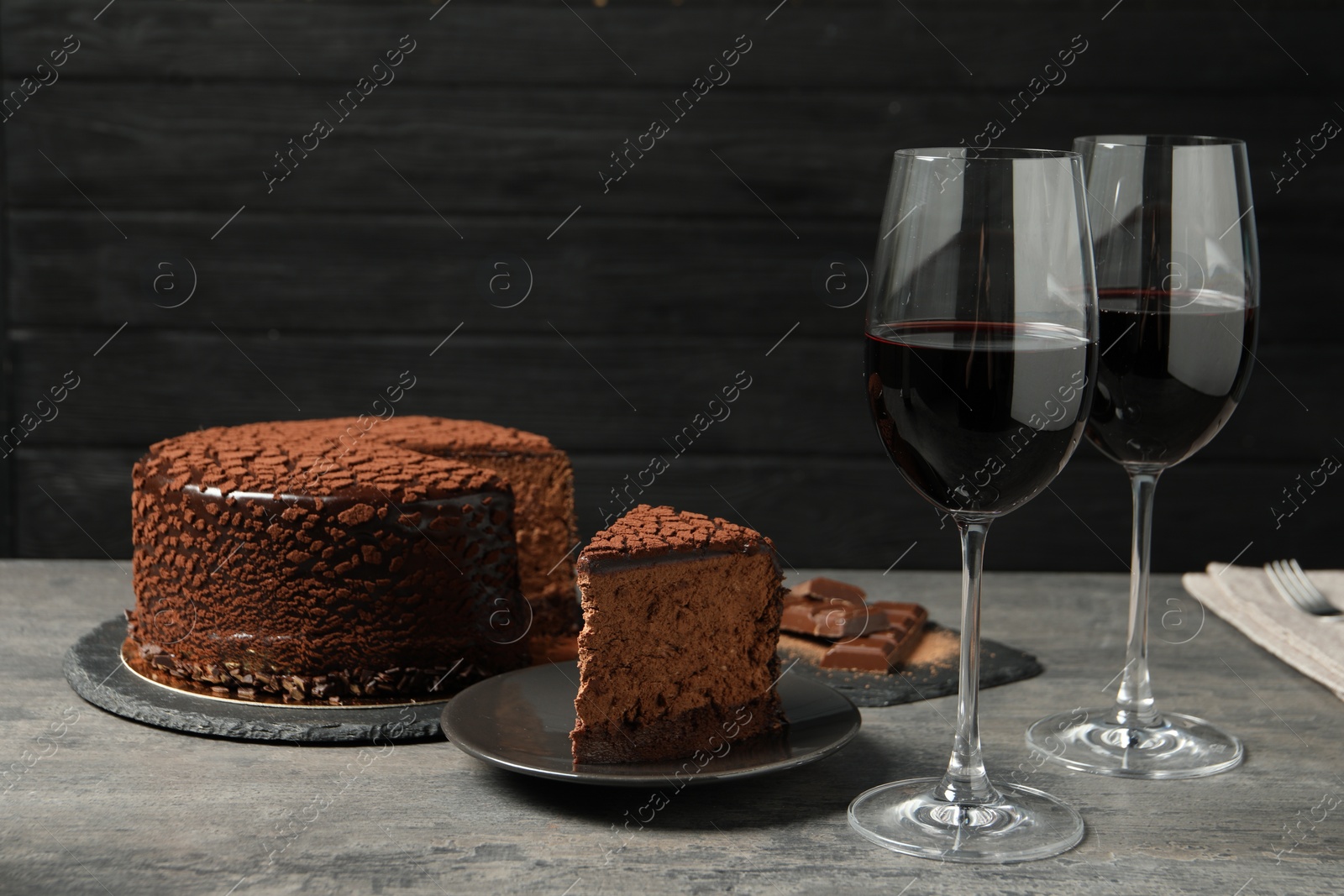 Photo of Delicious chocolate truffle cake and red wine on grey textured table