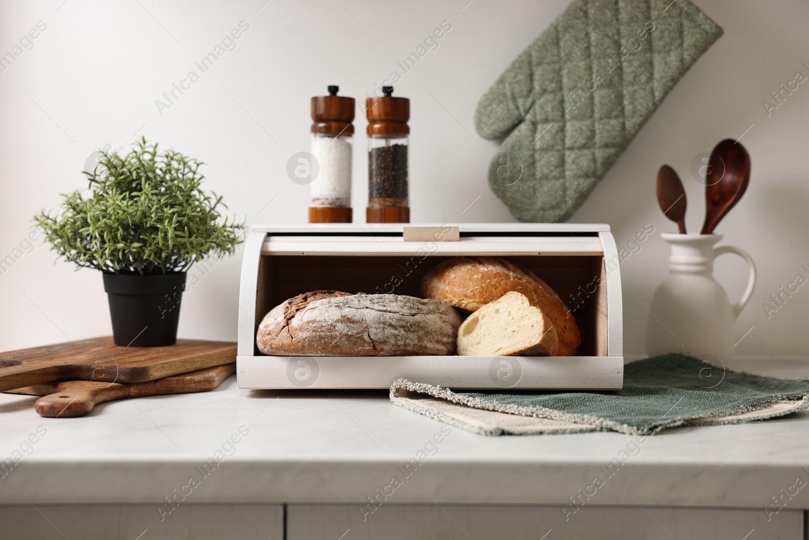 Photo of Wooden bread basket with freshly baked loaves on white marble table in kitchen