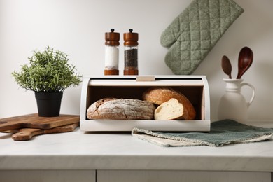 Wooden bread basket with freshly baked loaves on white marble table in kitchen