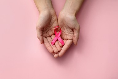 Woman holding pink ribbon on color background, top view with space for text. Breast cancer awareness concept