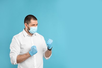 Photo of Man with protective mask and gloves in fighting pose on light blue background, space for text. Strong immunity concept