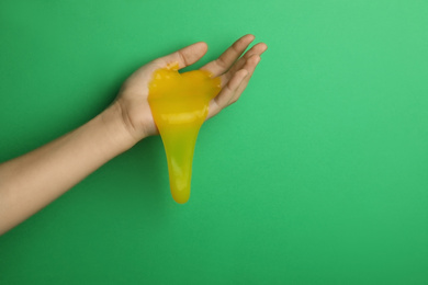 Photo of Woman playing with yellow slime on green background, closeup. Antistress toy