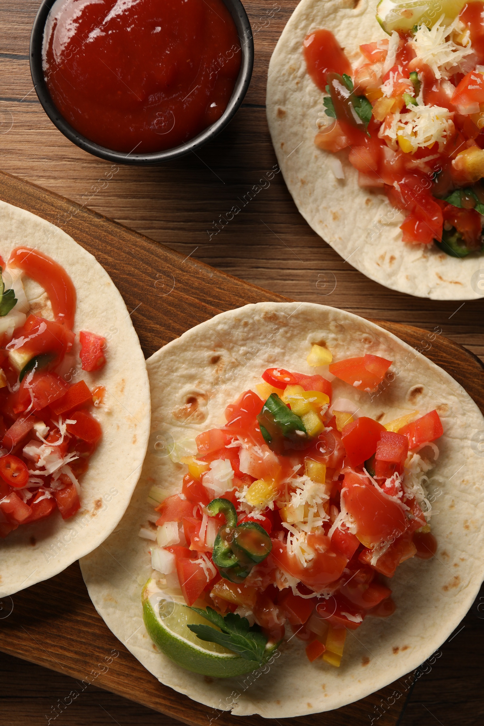 Photo of Delicious tacos with vegetables, lime and ketchup on wooden table, flat lay