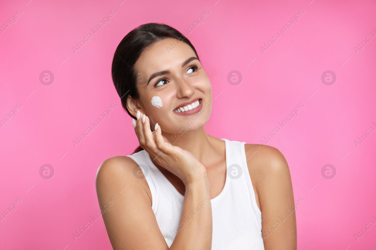 Photo of Young woman applying facial cream on pink background