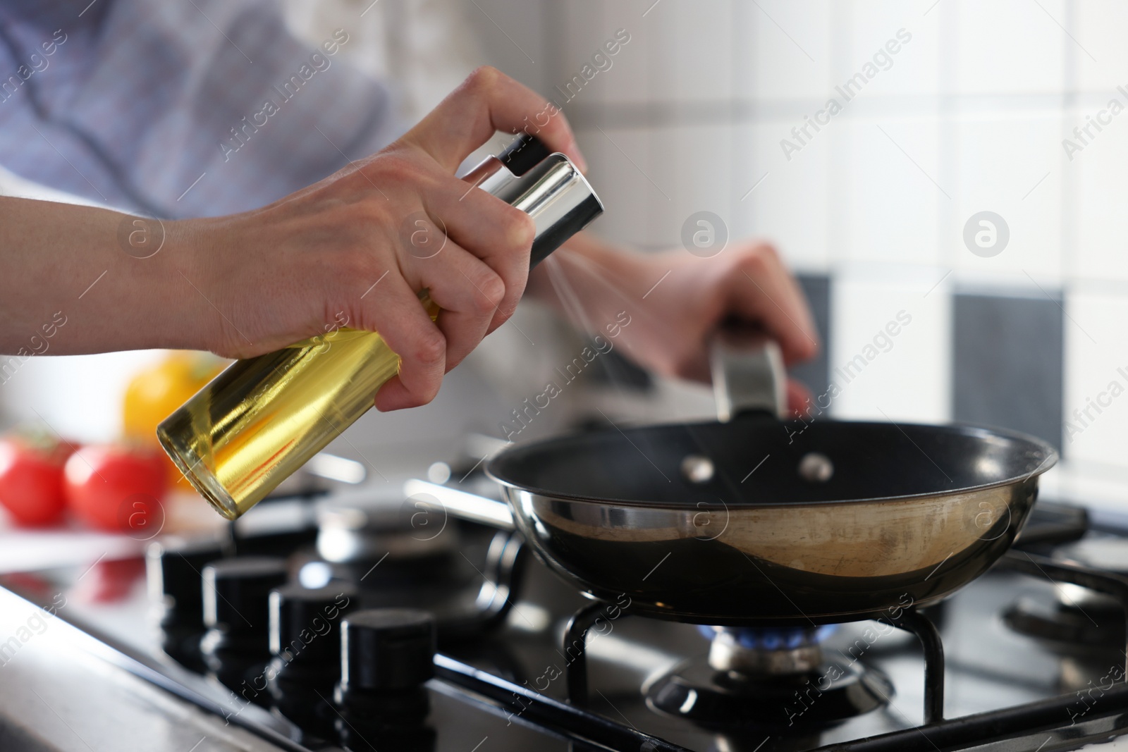 Photo of Vegetable fats. Woman sprinkling oil into frying pan on stove in kitchen, closeup