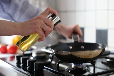 Vegetable fats. Woman sprinkling oil into frying pan on stove in kitchen, closeup