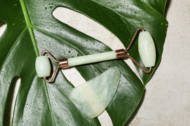 Gua sha stone, face roller and monstera leaf on light table, flat lay