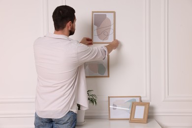 Photo of Man hanging picture frame on white wall at home