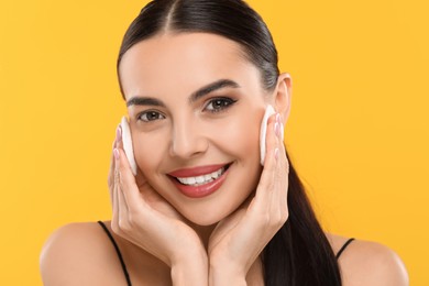 Beautiful woman removing makeup with cotton pads on orange background