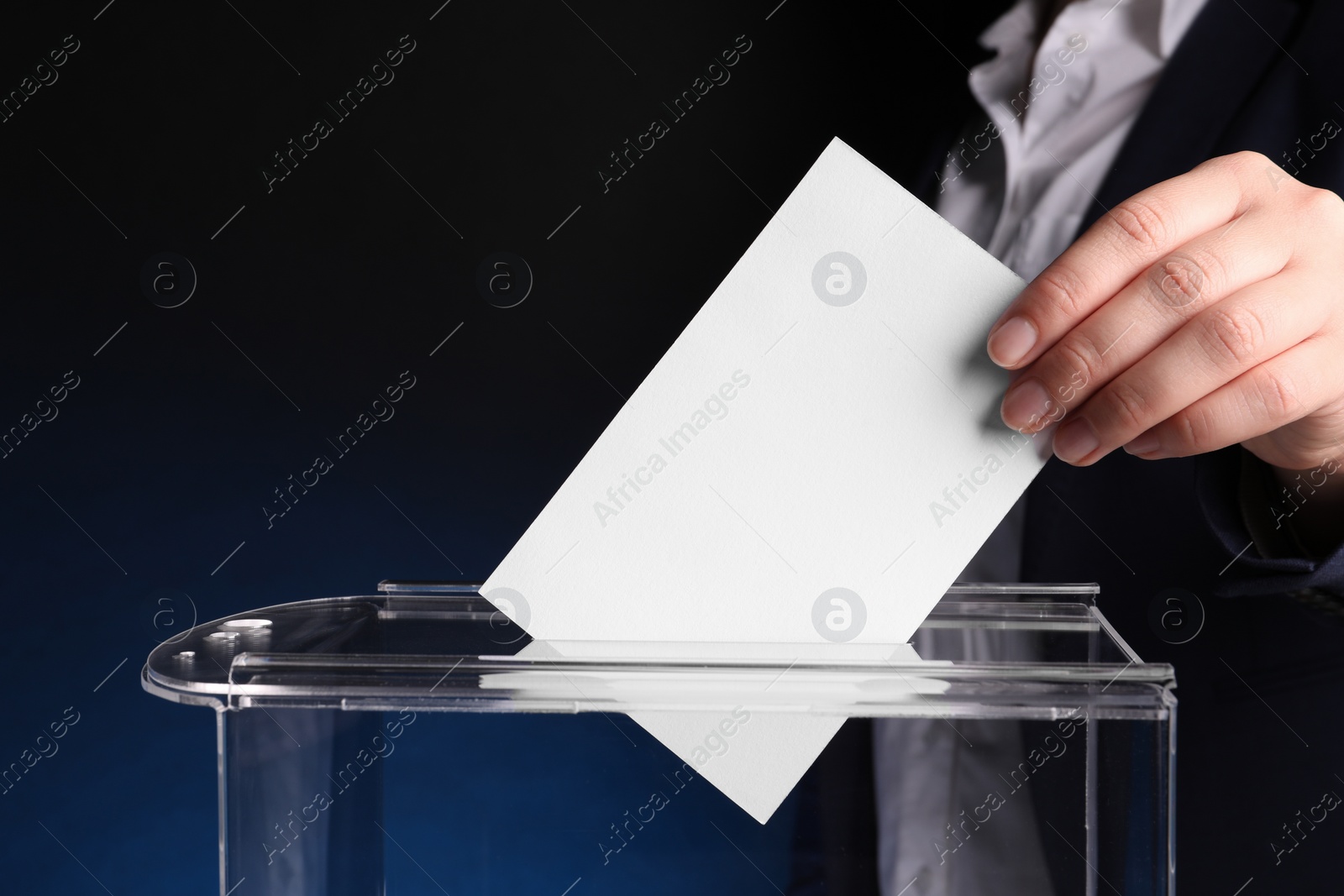 Photo of Woman putting her vote into ballot box on dark blue background, closeup