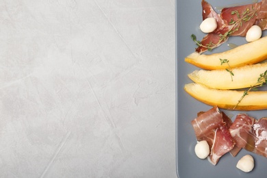 Photo of Plate of melon slices, mozzarella and prosciutto on gray background, top view. Space for text