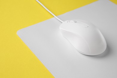 Photo of One wired mouse with mousepad on yellow background, closeup