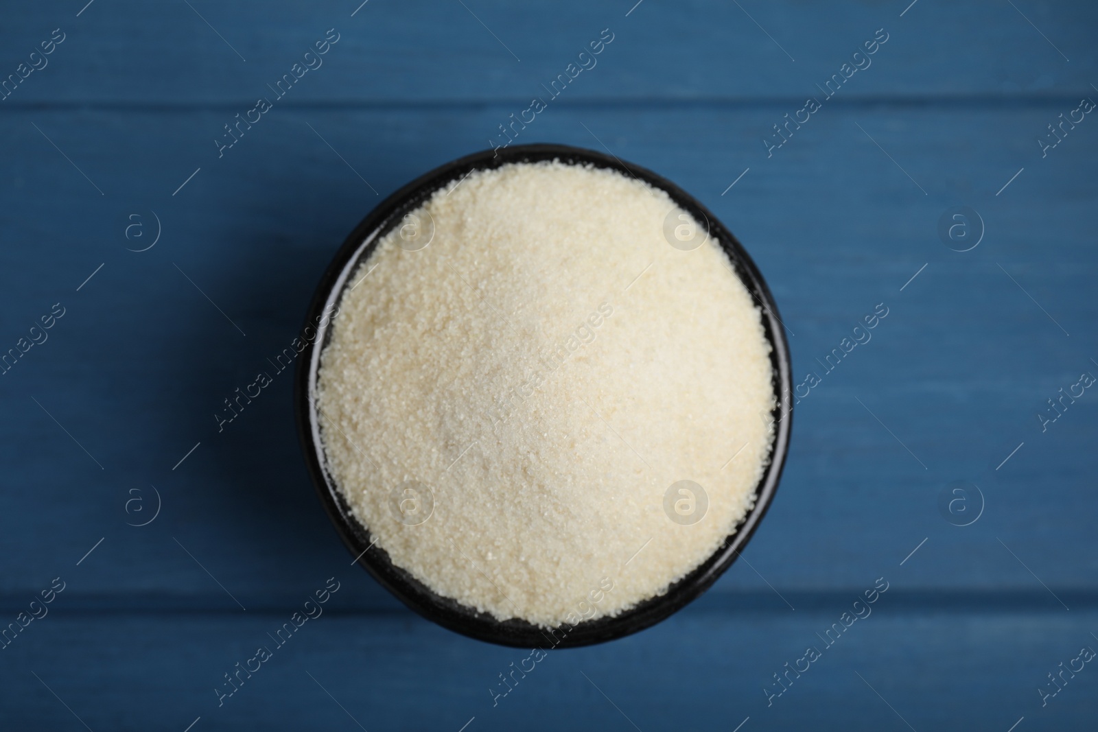 Photo of Gelatin powder in bowl on blue wooden table, top view