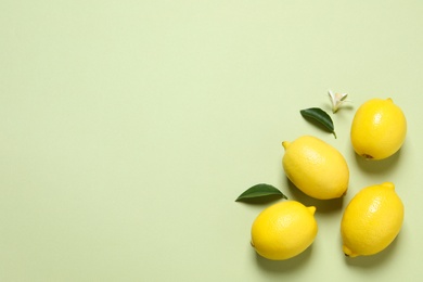 Fresh ripe lemons and leaves on light green background, flat lay with space for text