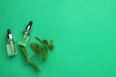 Photo of Bottles of essential oil and mint on green background, flat lay. Space for text