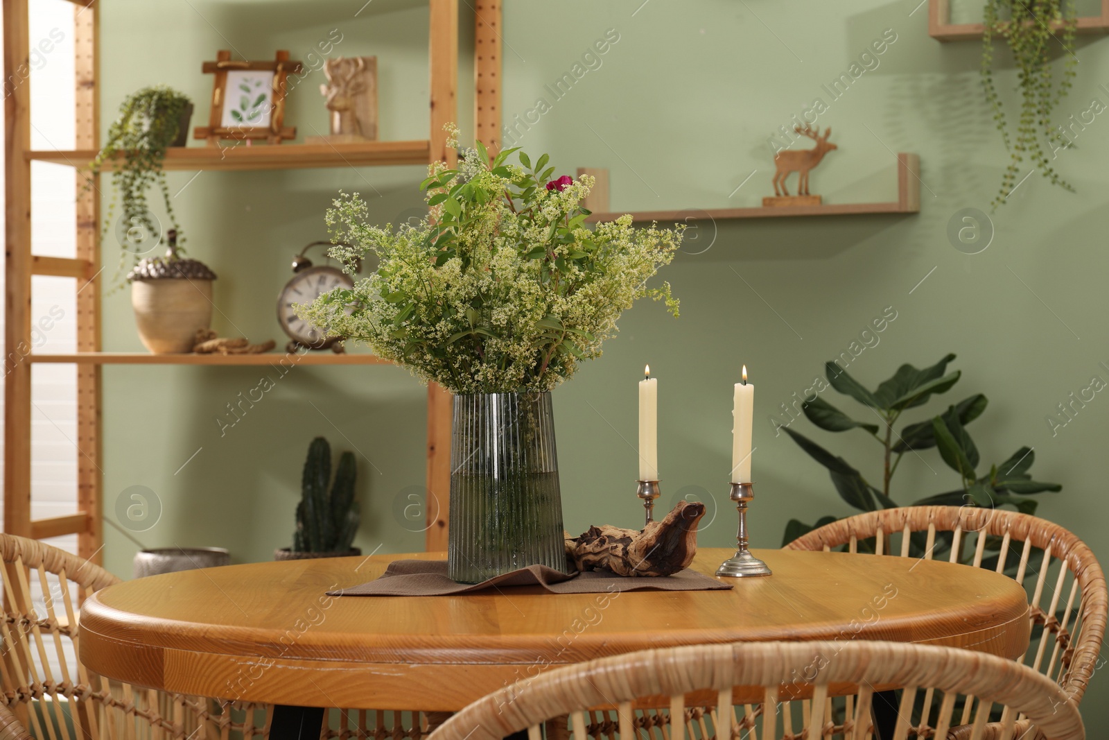 Photo of Vase with beautiful flowers and candles on wooden table in stylish dining room