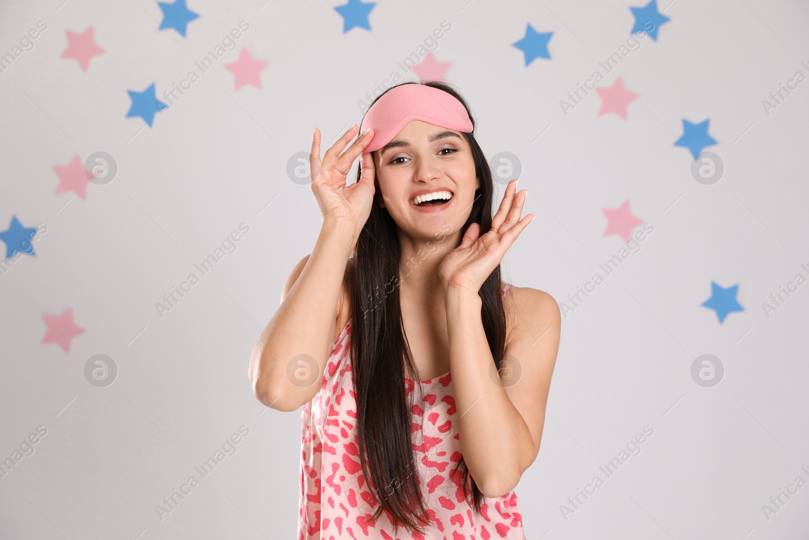 Photo of Beautiful woman wearing sleeping mask on light grey background. Bedtime