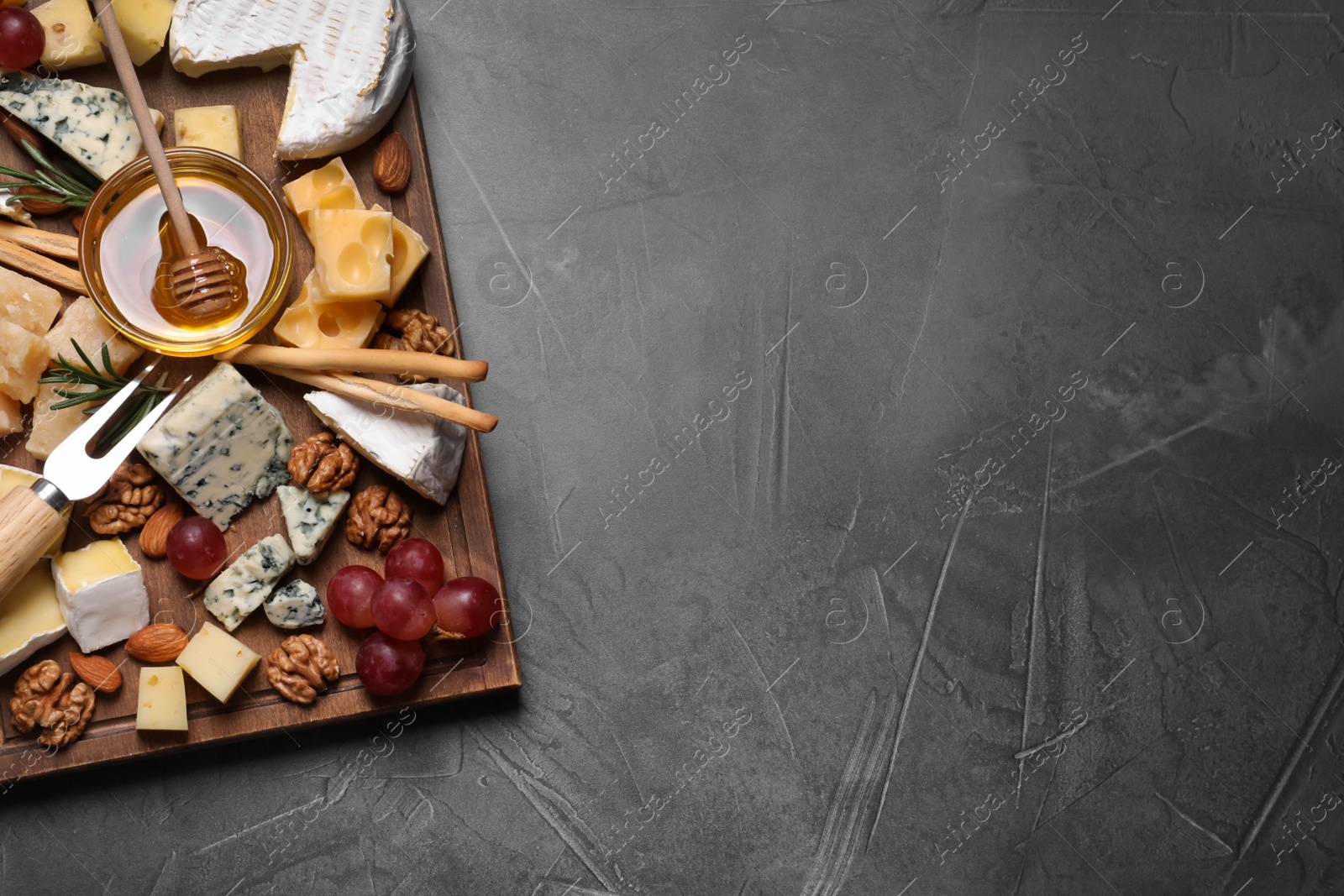 Photo of Cheese plate with honey, grapes and nuts on grey table, top view. Space for text