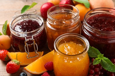 Photo of Jars with different jams and fresh fruits on wooden table, closeup