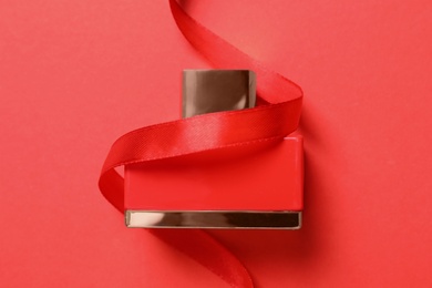 Photo of Bottle of perfume with ribbon on red background, top view