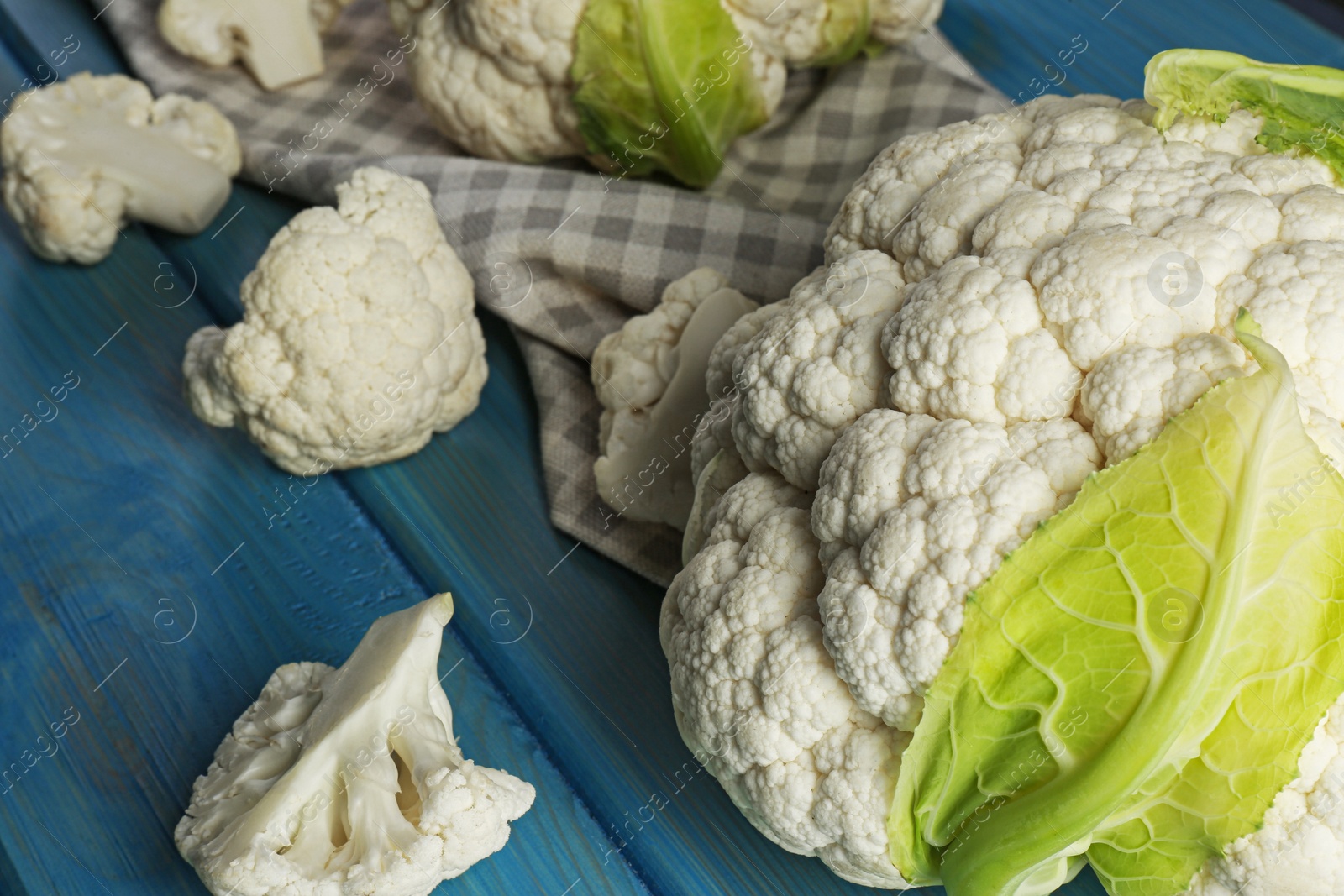 Photo of Fresh whole and cut cauliflowers on light blue wooden table, closeup