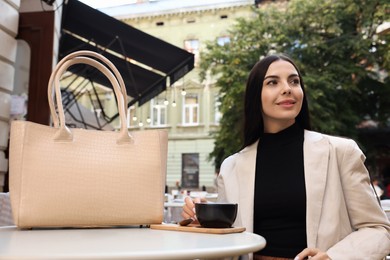 Photo of Young woman with stylish bag at table in outdoor cafe