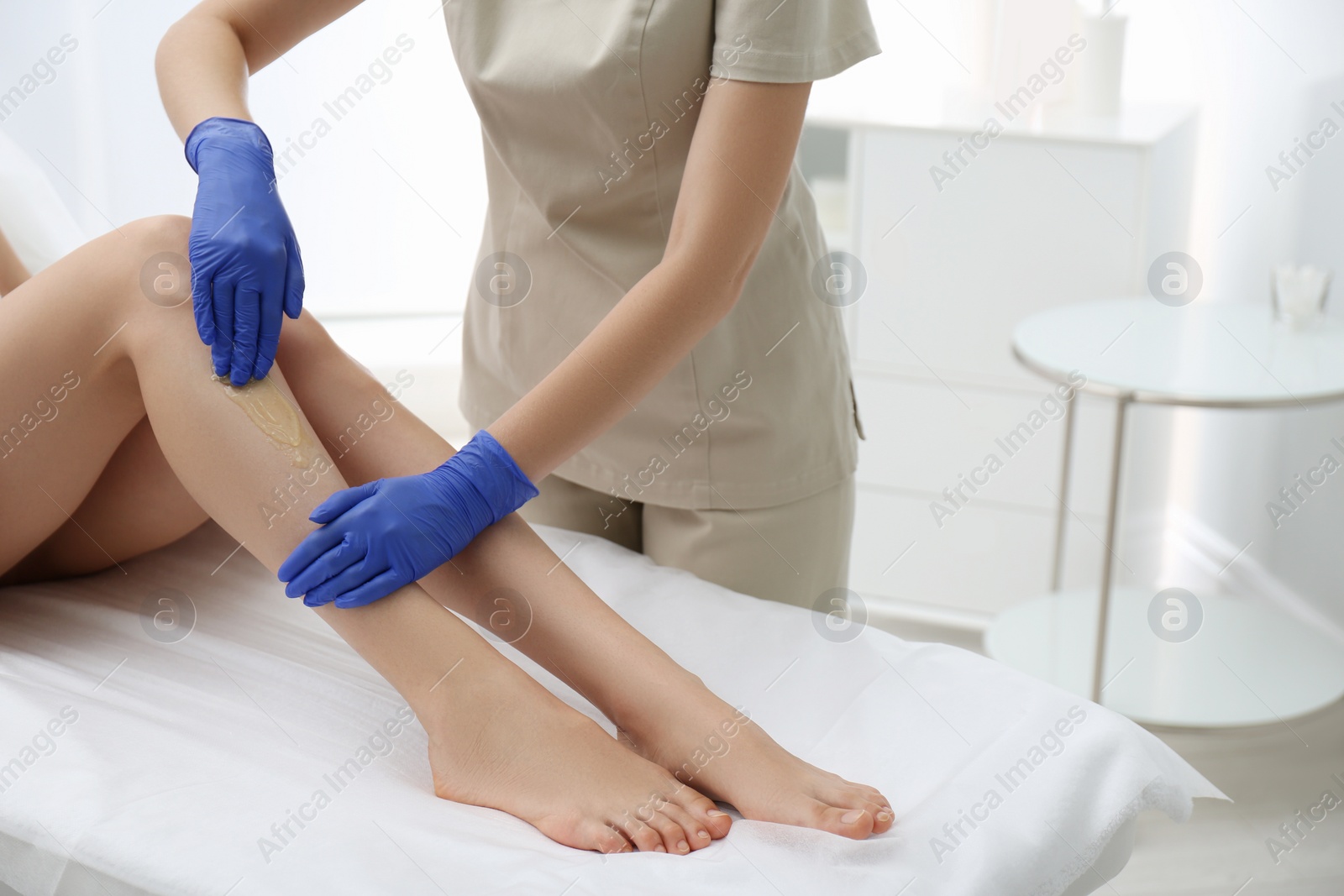 Photo of Woman getting wax epilation of legs in salon, closeup